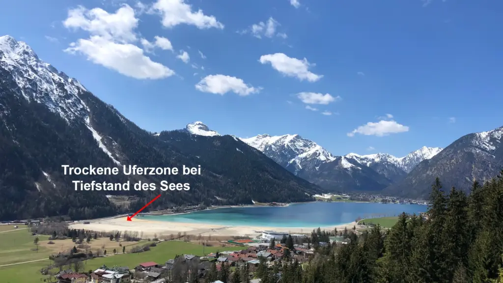 Bergsee mit trockener Uferzone und Dorf im Vordergrund