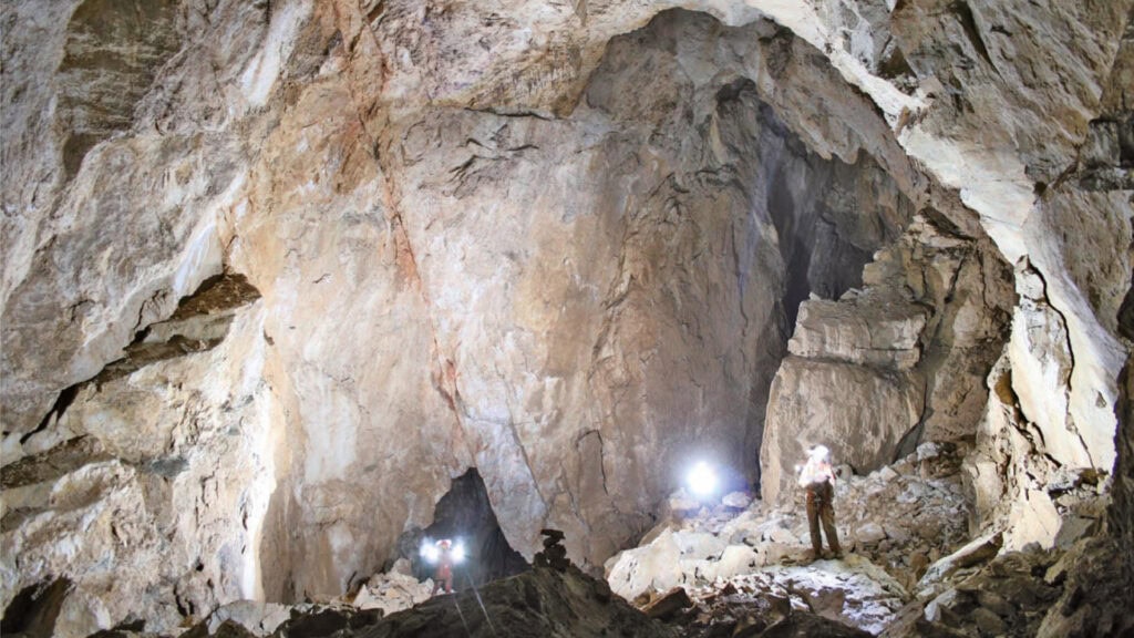 Personen erkunden beleuchtete Höhle mit Felsenwand.