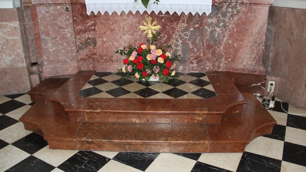 Altar mit Blumenarrangement vor Marmorwand.