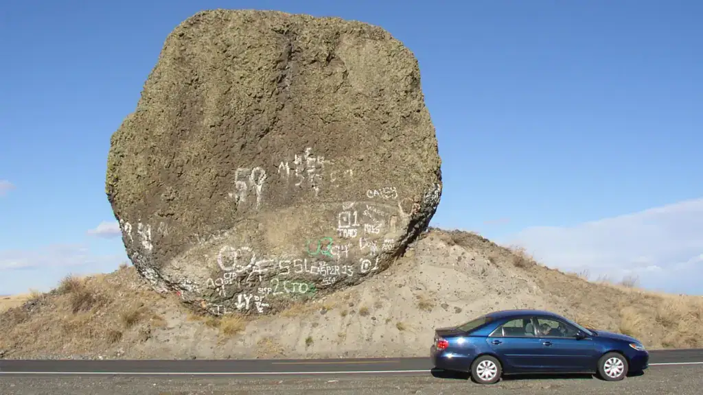 Auto vor riesigem Felsen mit Graffiti.